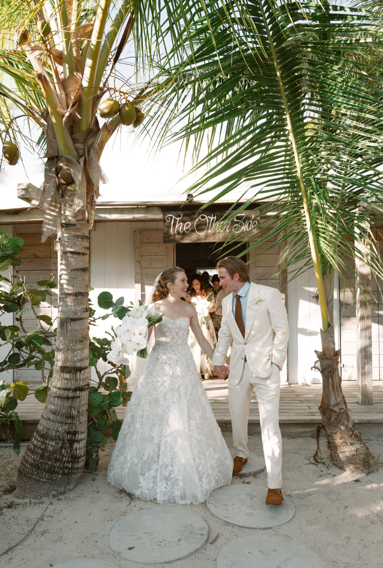 Bride and groom hold hands under palm trees.