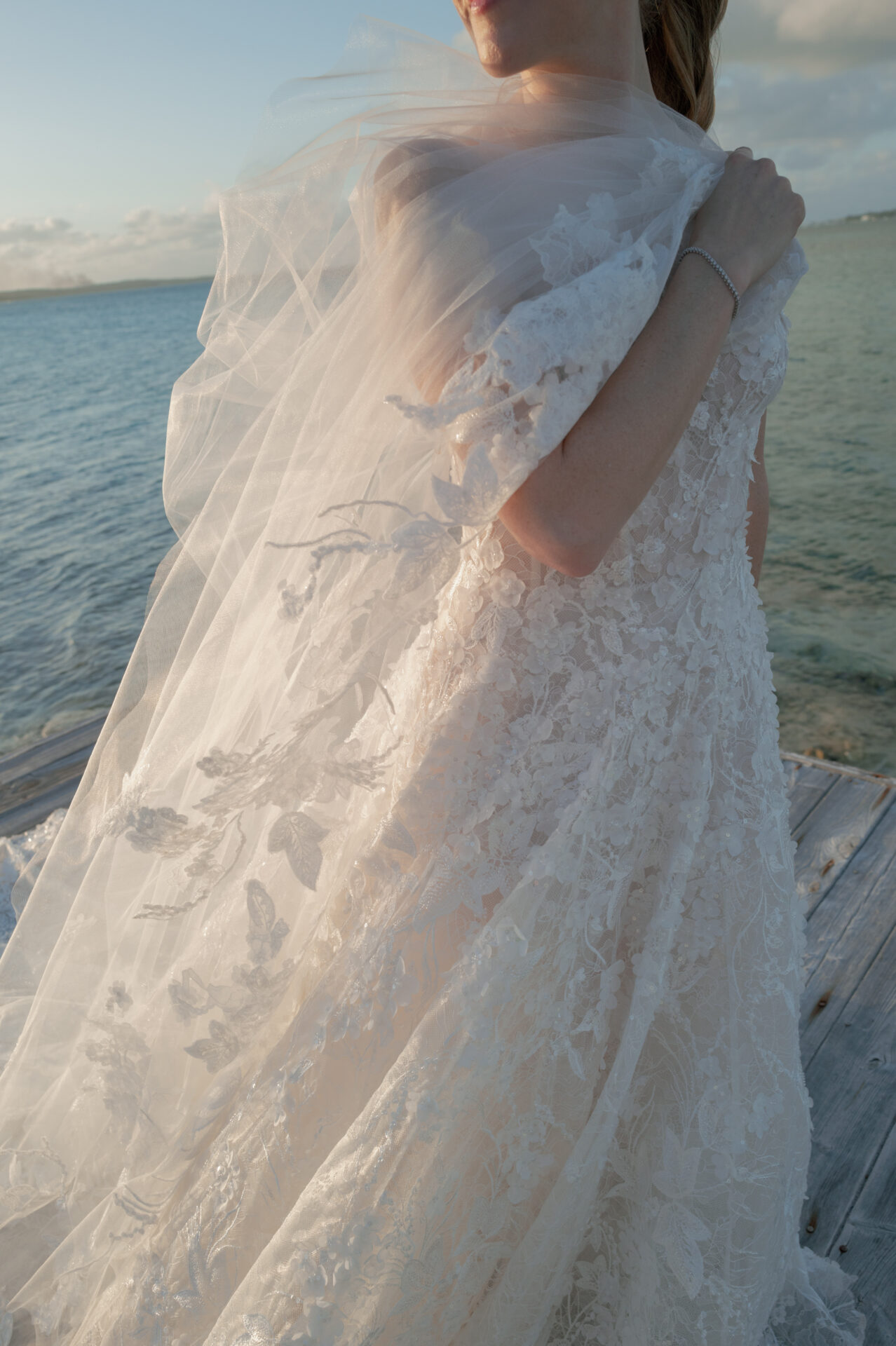 Bride on dock in lace dress, sunlight on veil.