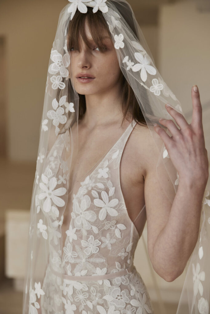 Woman in sheer floral wedding dress, hand partially raised.