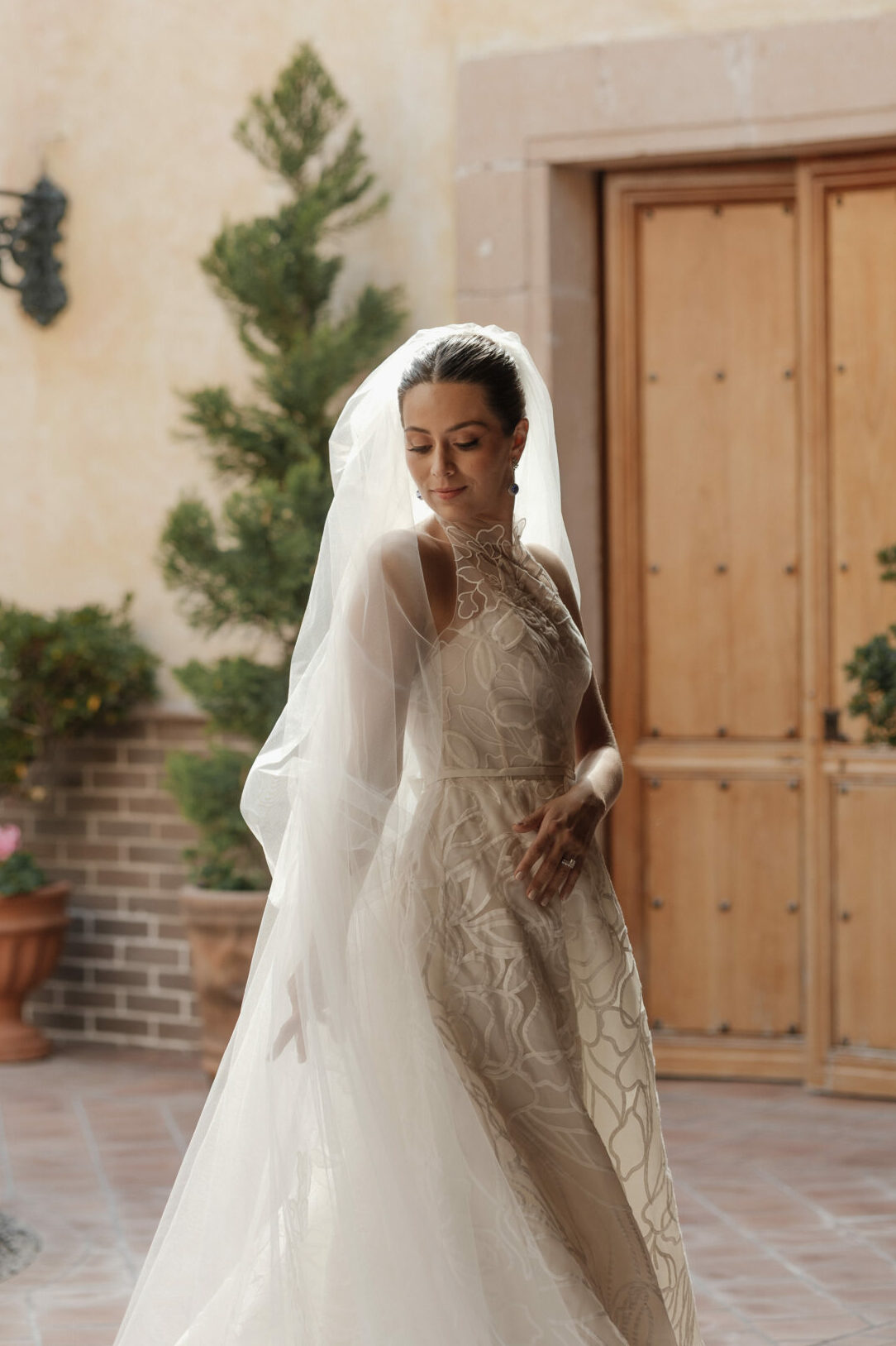 Bride in A-line gown stands in sunlit courtyard.