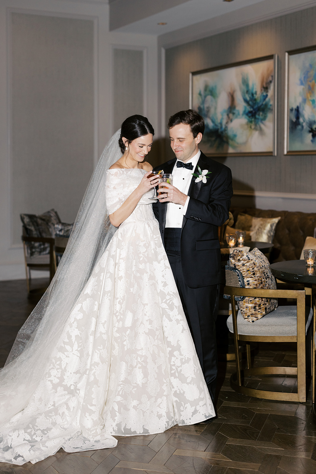 Bride and groom in elegant room, smiling with drinks.