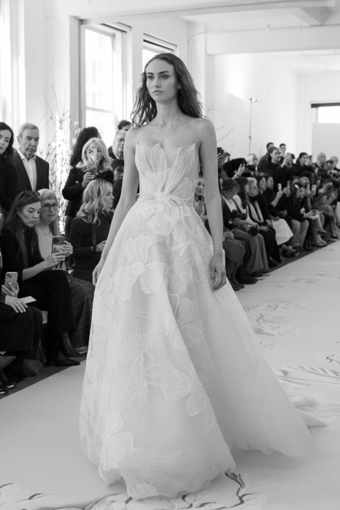 Model in floral gown on black-and-white runway.