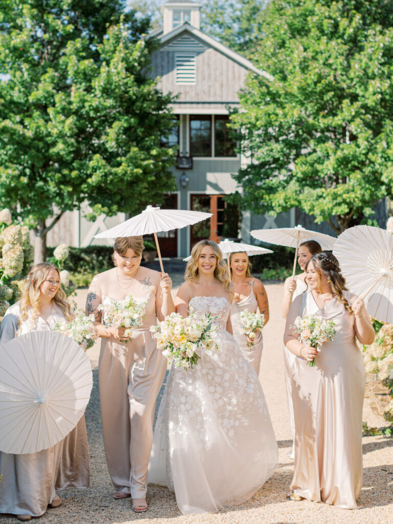 Bride and bridesmaids smiling outdoors with parasols.