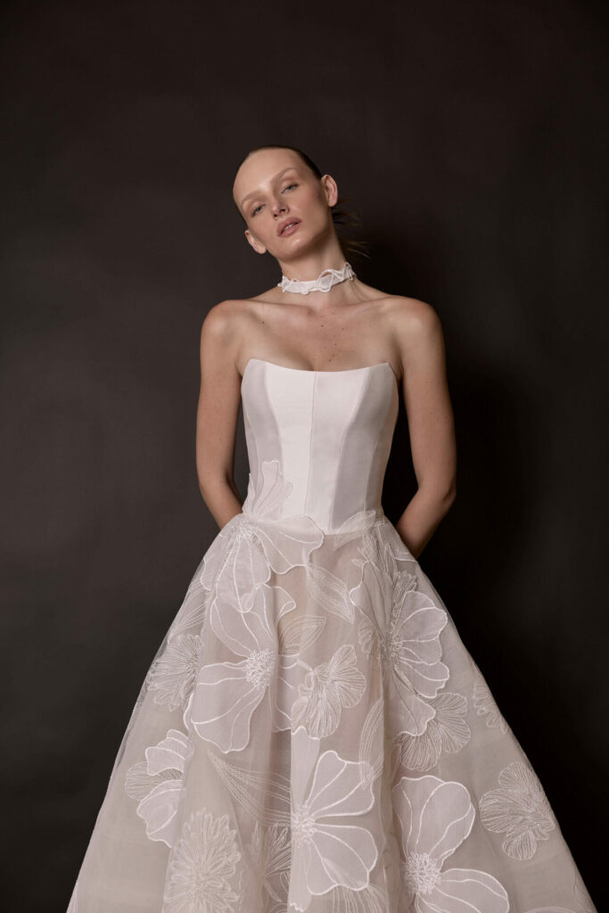 Woman in floral white gown and choker, dark background.