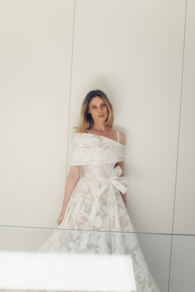 Woman in white floral off-shoulder gown poses calmly.