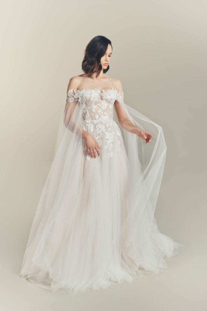 Woman in sheer white floral gown looks down.