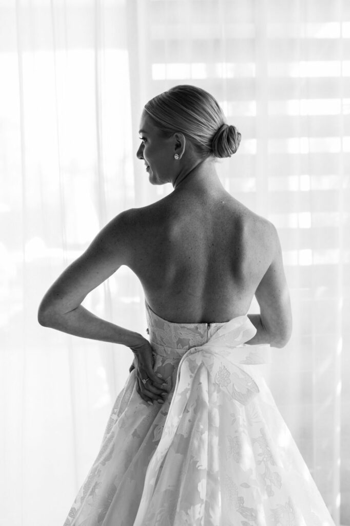 Bride in Mira Zwillinger gown with bow, backlit.