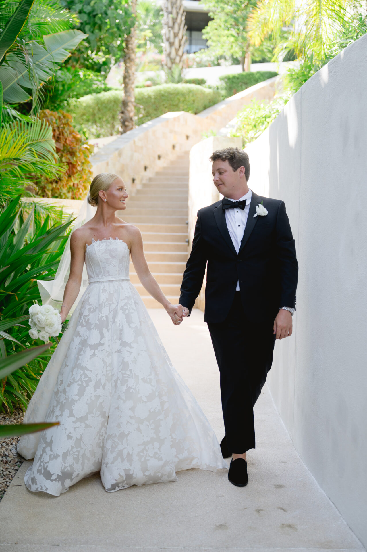 Bride and groom in luxury attire walk outdoors.