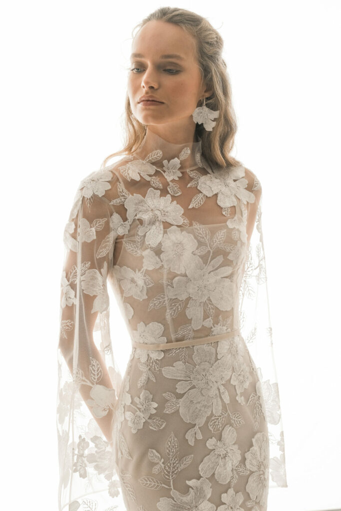 Woman in floral embroidered white dress, looking down.