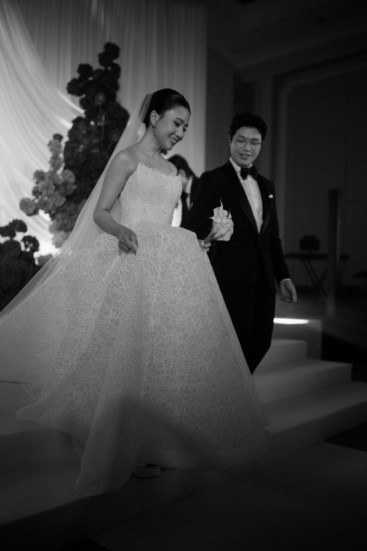 Bride and groom descend steps, black-and-white scene.