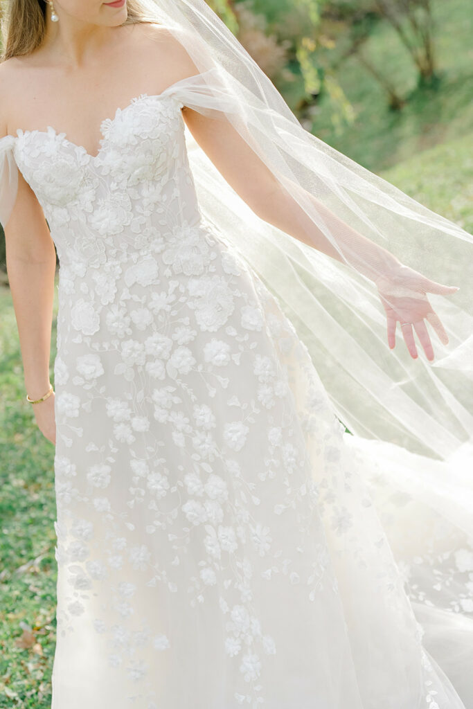 Bride in white lace gown outdoors, sunlight shining.