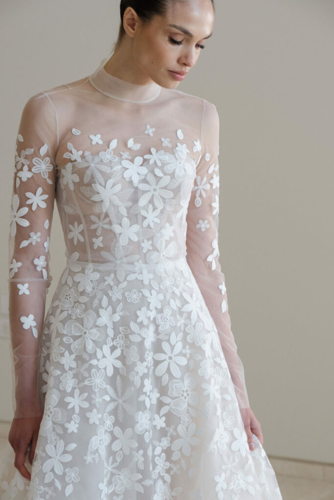 Woman in sheer, embroidered white dress looks down.