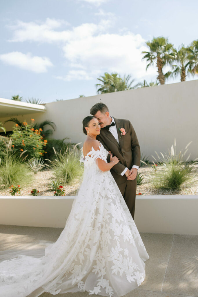 Bride and groom embrace outdoors among palm trees.