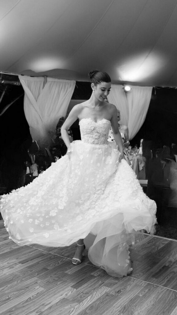 Smiling woman twirls in floral gown, black-and-white.