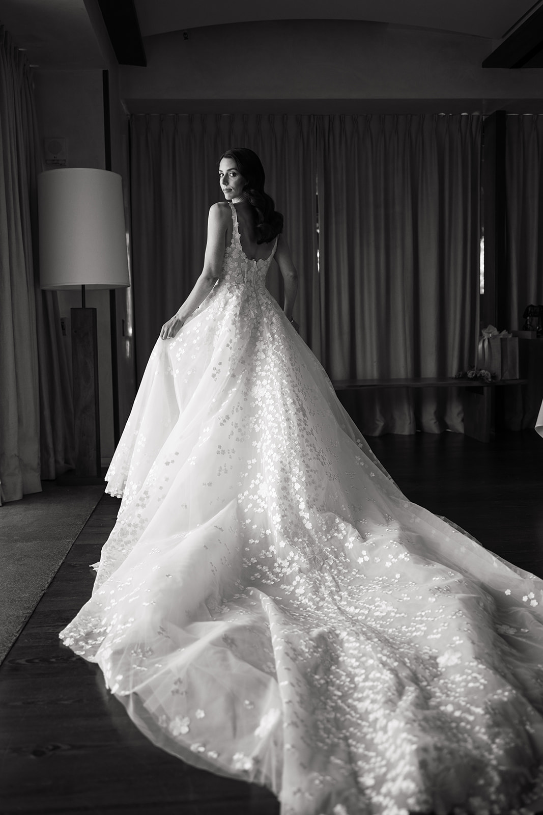 Woman in floral wedding gown, softly lit indoors.