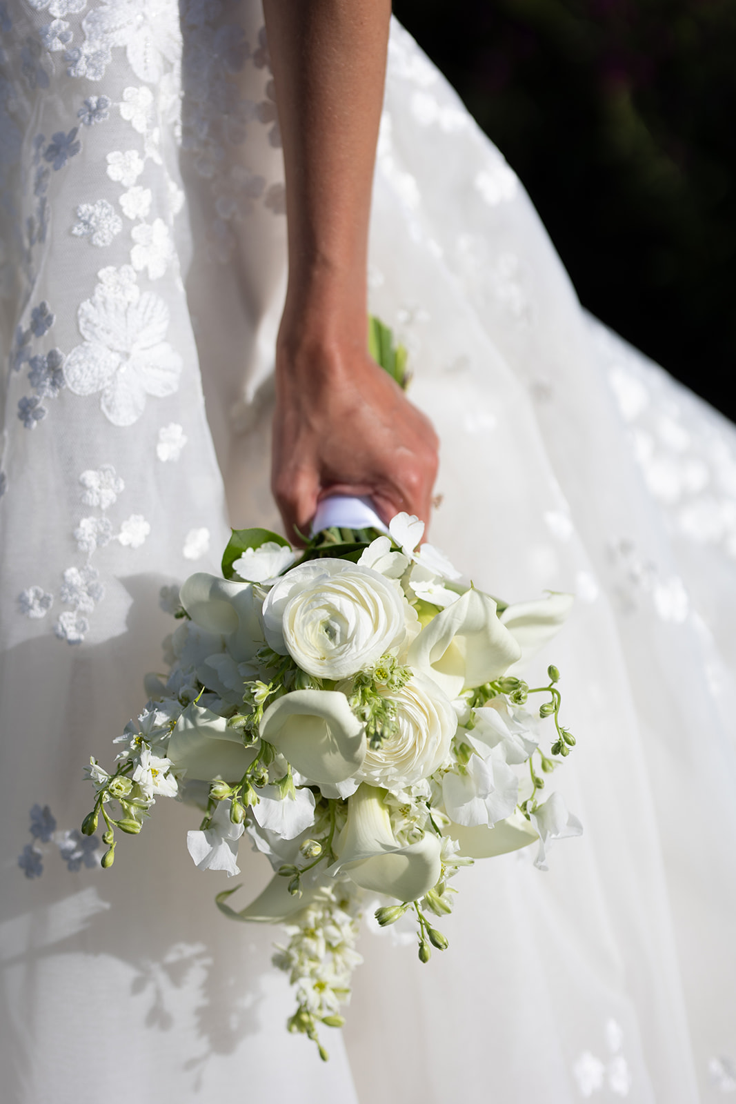 Bride in lace dress holds bouquet, sunlight shines.
