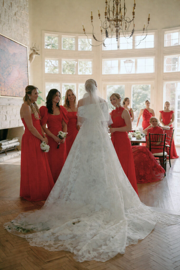 Bride poses in couture gown with bridesmaids in red.