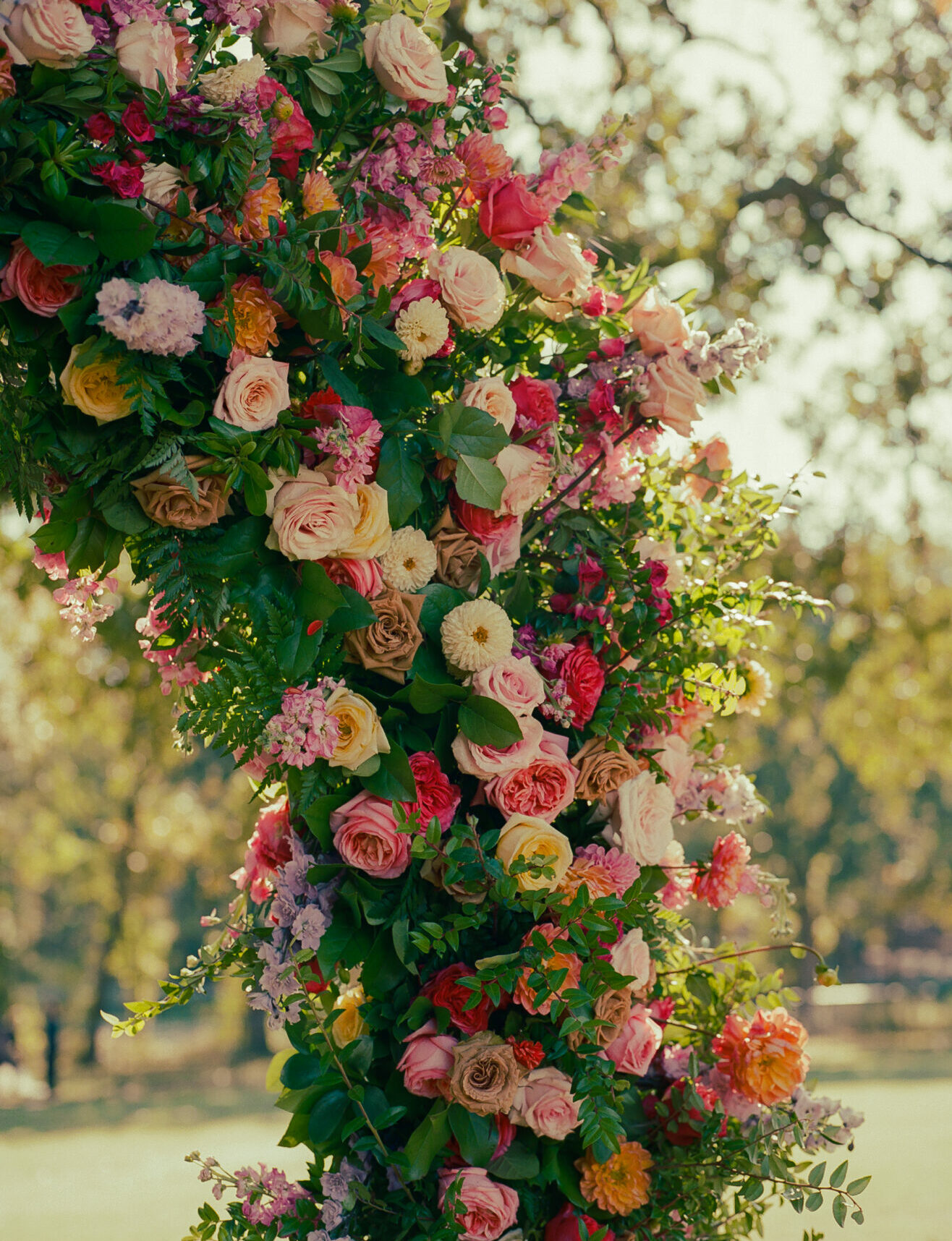 Curved floral display with pink, peach, and cream roses outdoors.
