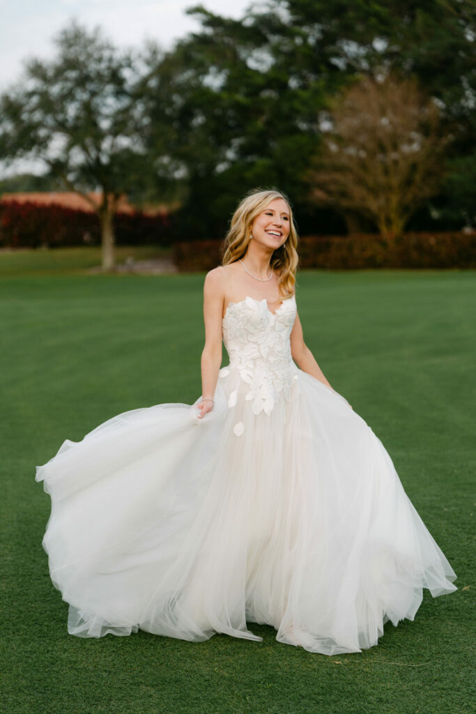 Woman in flowing gown smiles on grassy lawn.
