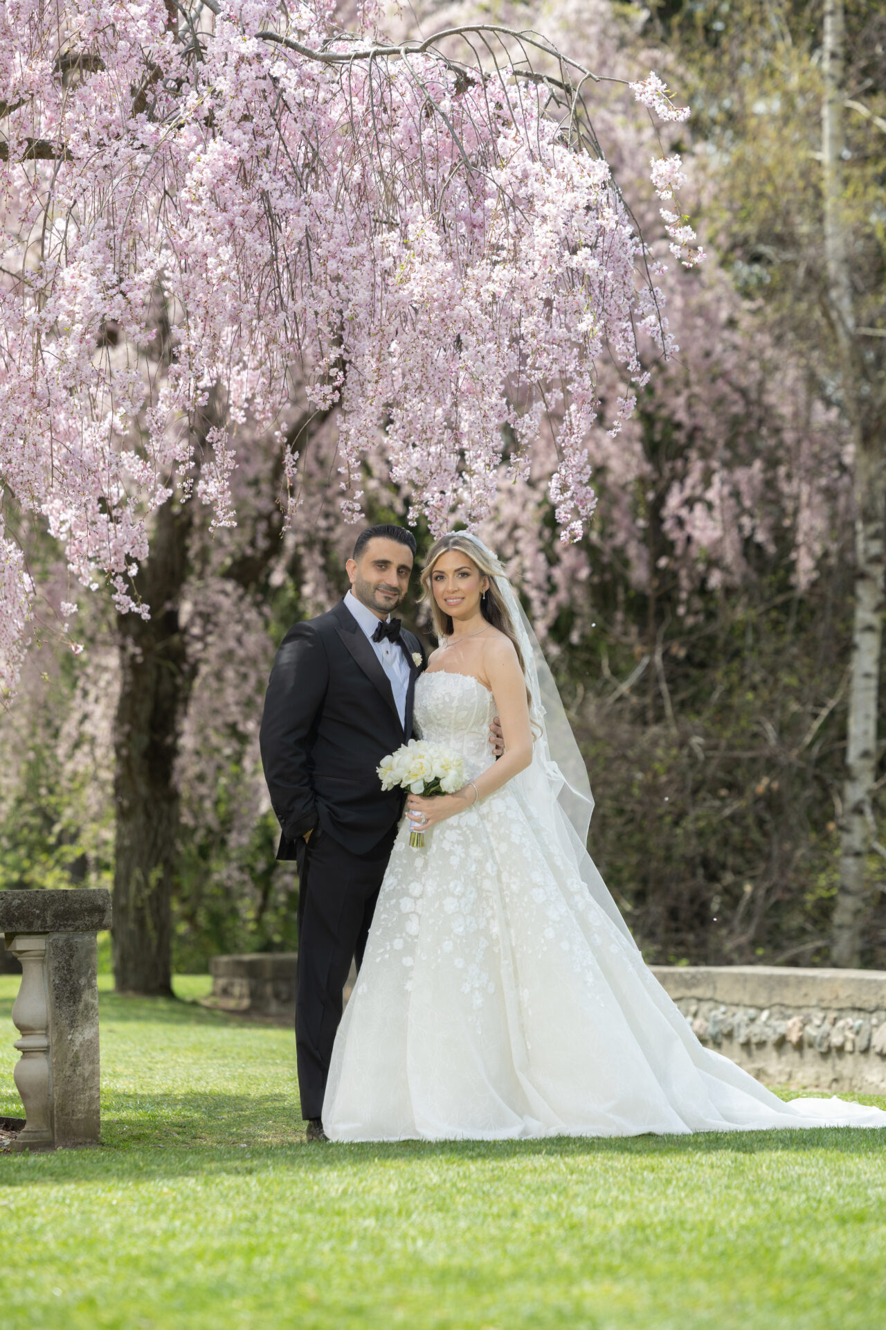 Bride and groom under pink cherry blossoms outdoors.