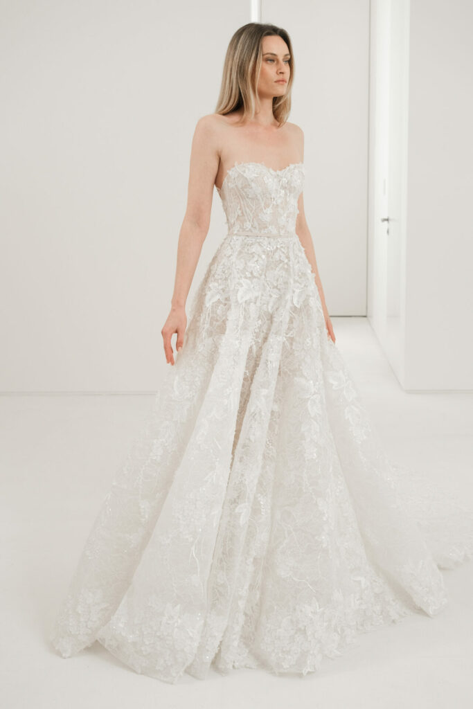 Woman in strapless white lace gown, minimalist room.