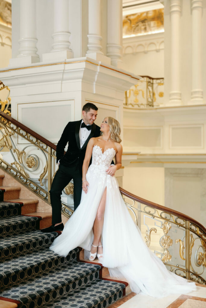 Bride and groom gaze lovingly on grand staircase.