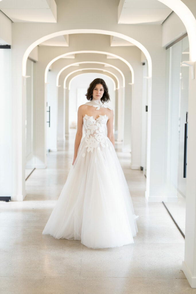 Woman in white floral wedding dress, bright hallway.