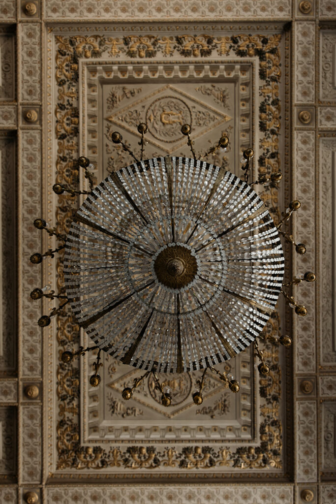 Opulent crystal chandelier under ornate gold-ceiling splendor.