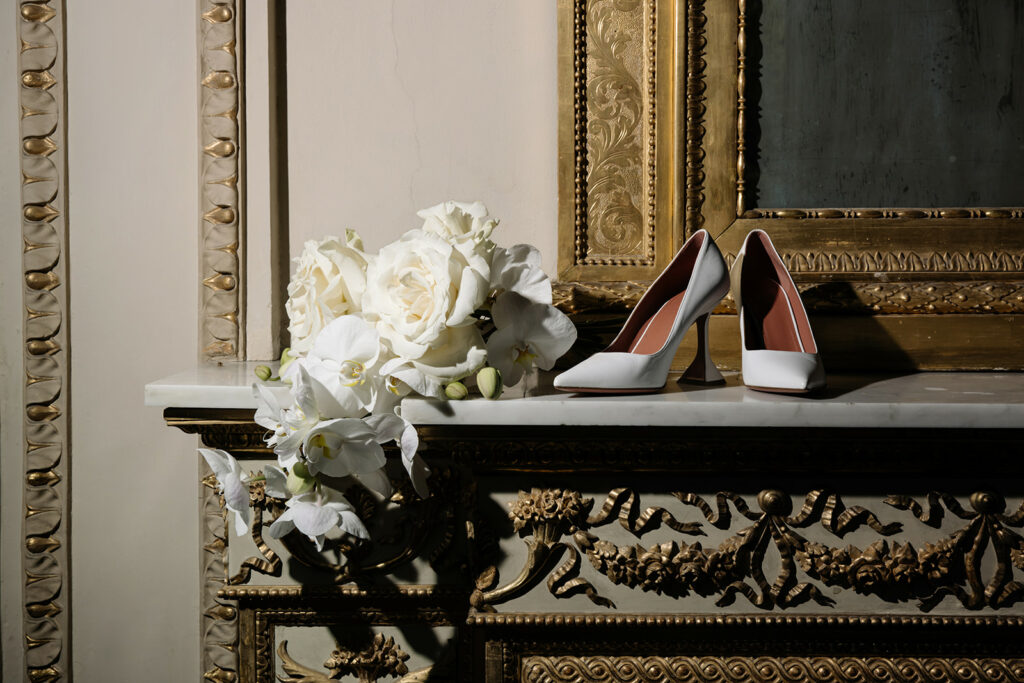 White heels and bouquet on gold-trimmed marble mantel.