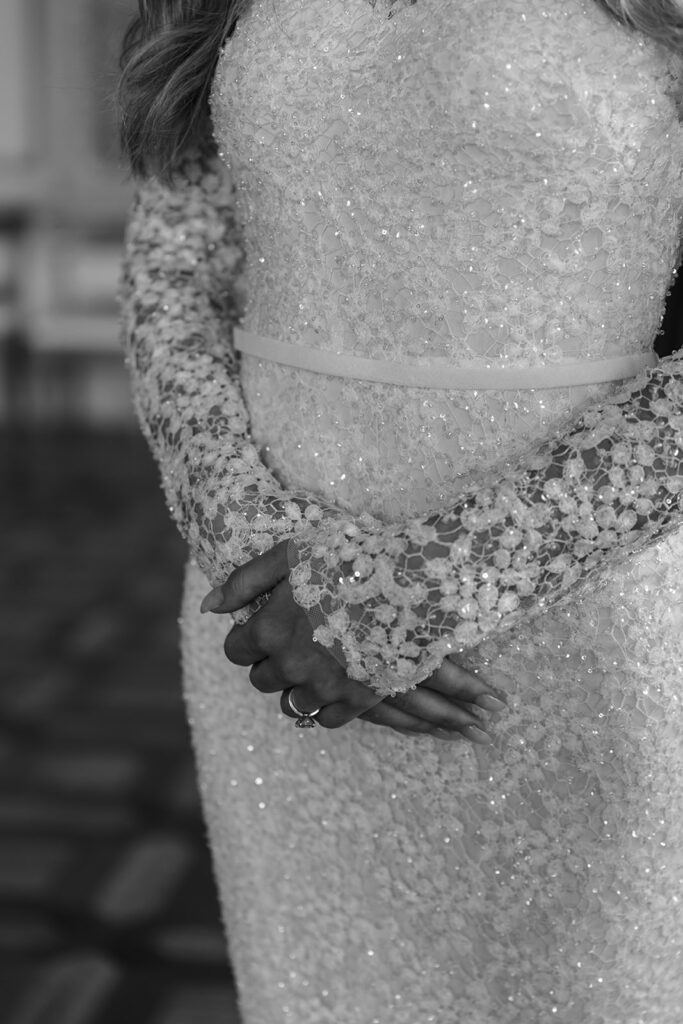 Woman in sparkling lace gown, hands clasped, face hidden.