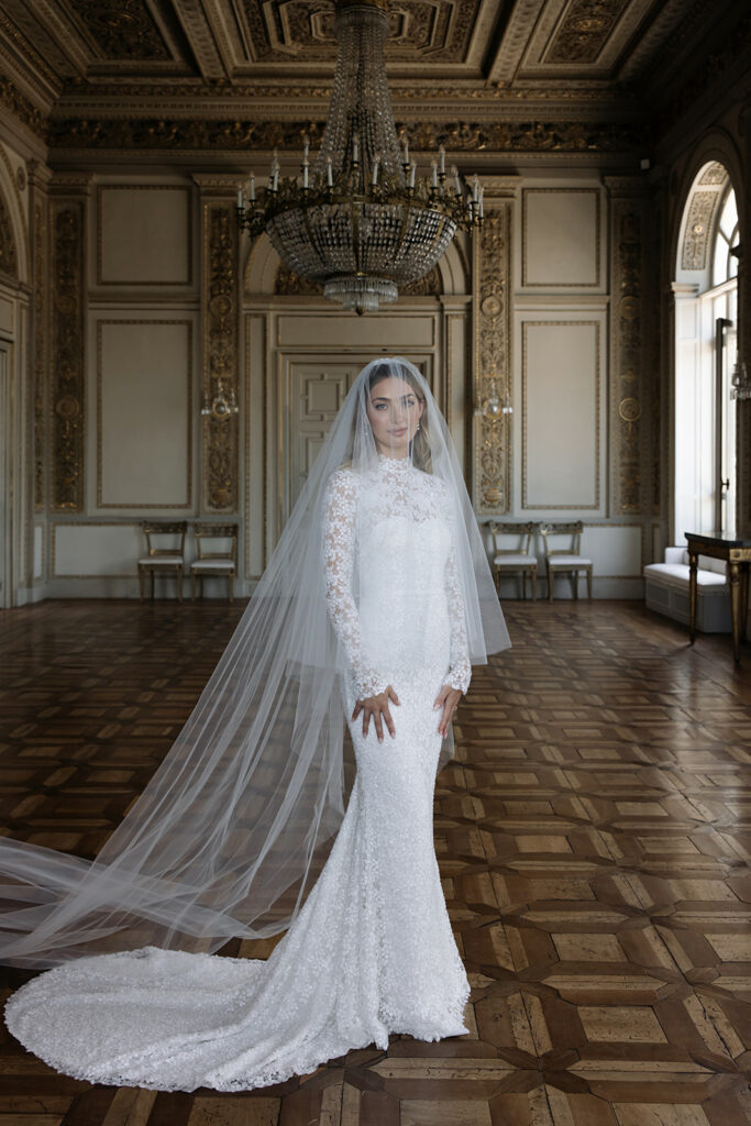 Bride in Mira Zwillinger gown beneath crystal chandelier.