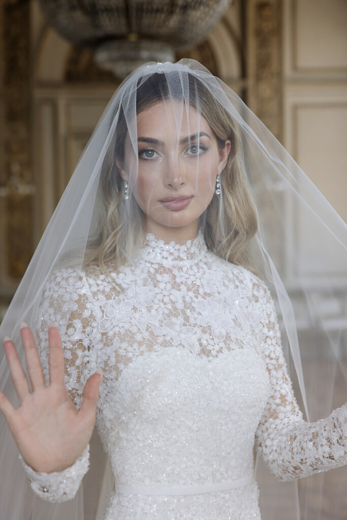 Katya Ruiz in lace Mira Zwillinger gown, luxe indoor setting.