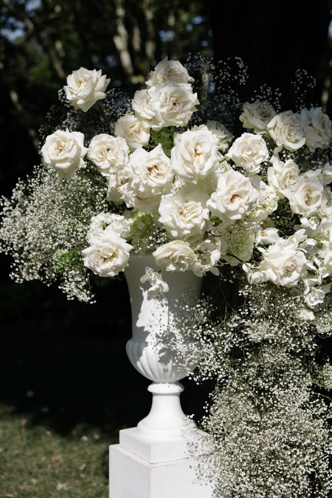 White urn with roses, baby's breath, outdoor sunlight.