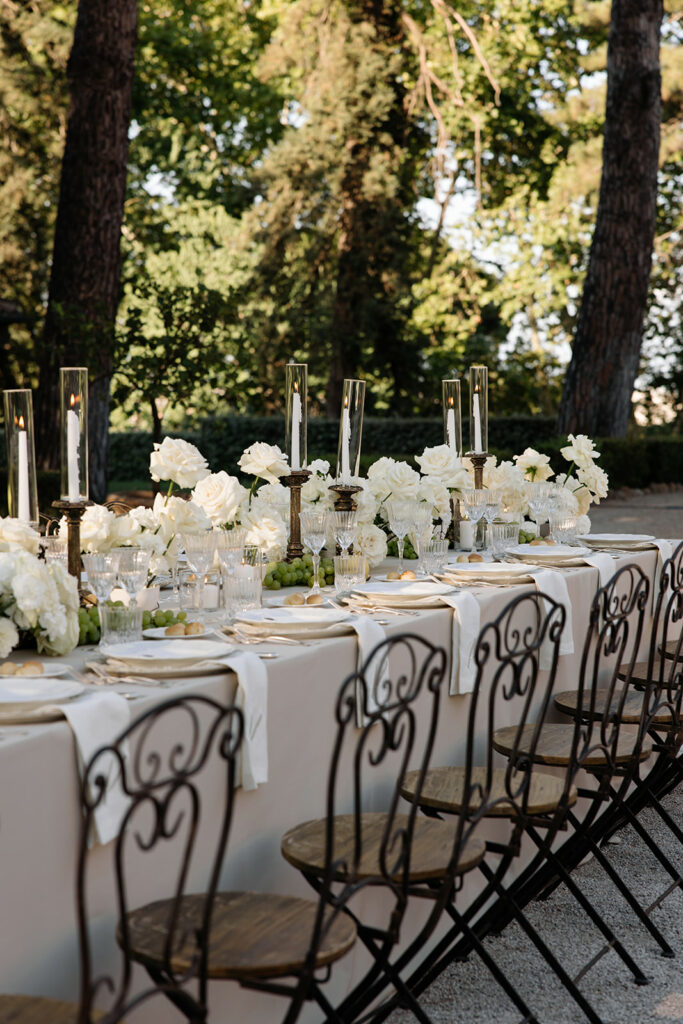 Chic outdoor table with white flowers, glassware, candles.