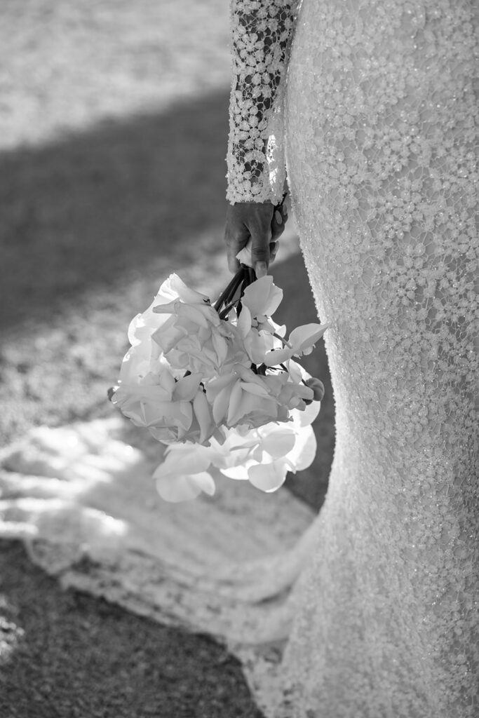 Bride in lace gown holds bouquet, dramatic shadows.