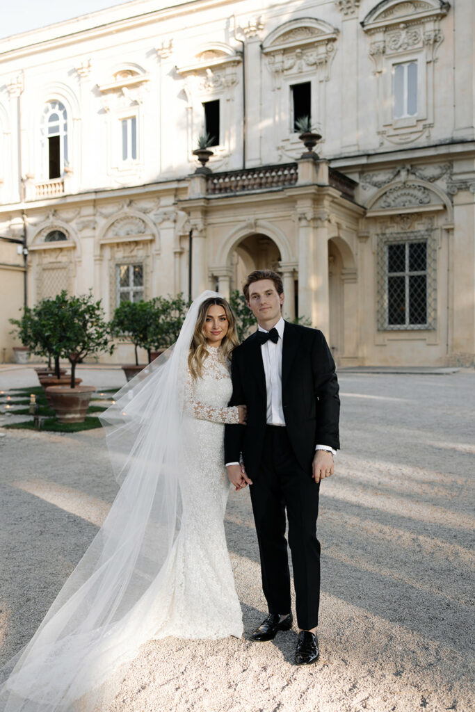 Bride in Amy gown, groom in tux, smiling outside.