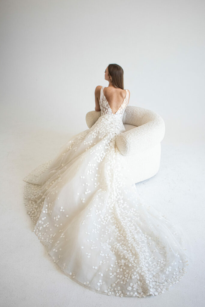 Woman in floral-embroidered wedding gown on white chair.