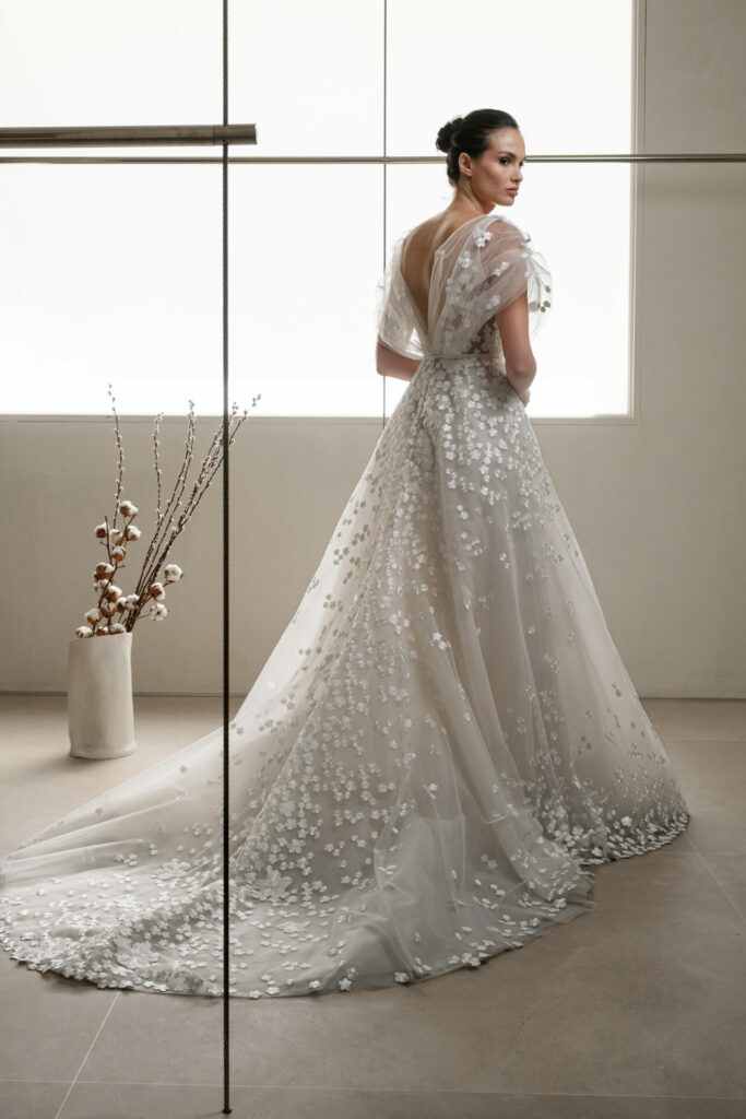 Woman in sheer white gown with floral appliqué.