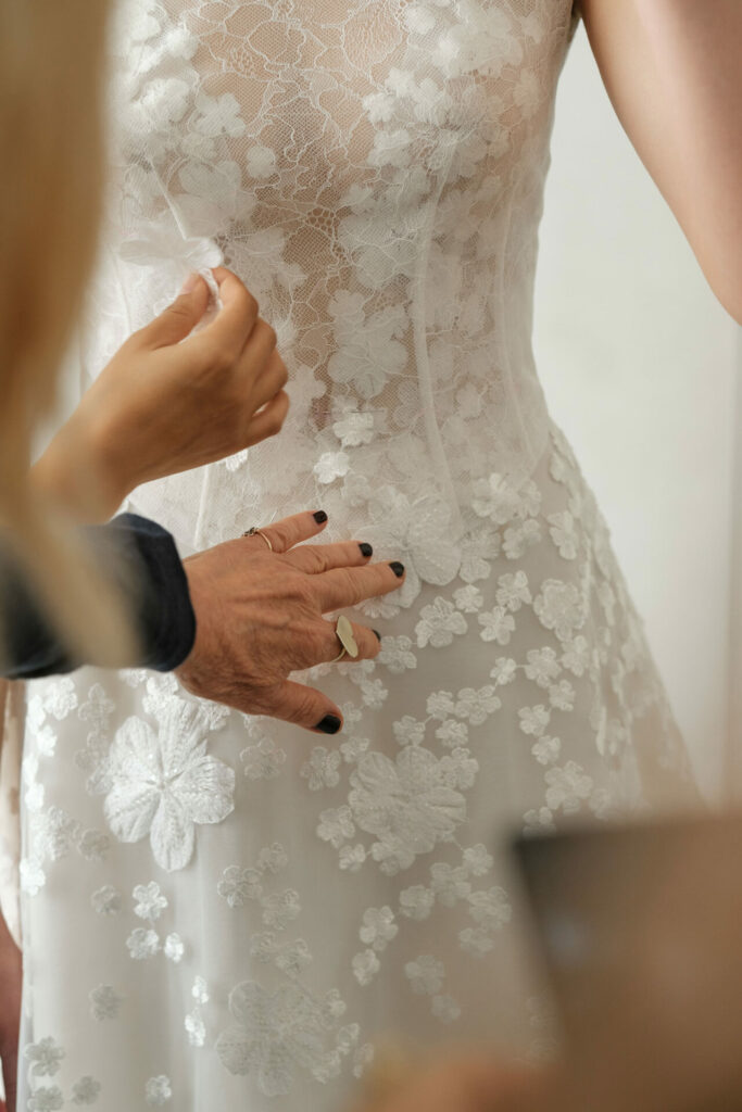 Hands adjust floral lace on wedding dress bodice.