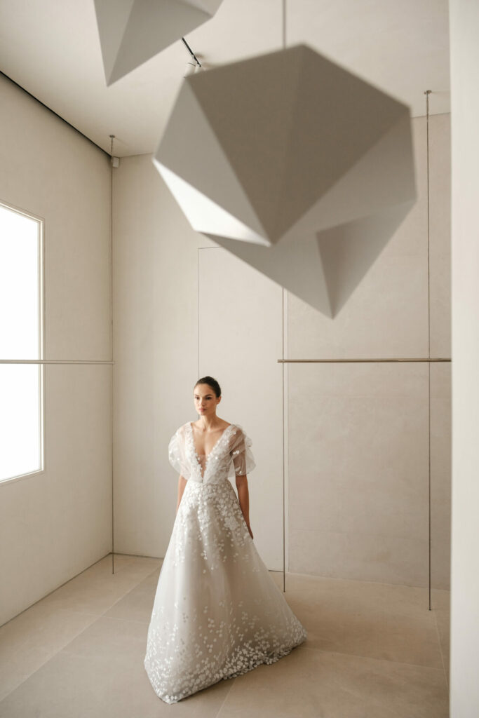 Woman in white floral gown in bright, minimal room.