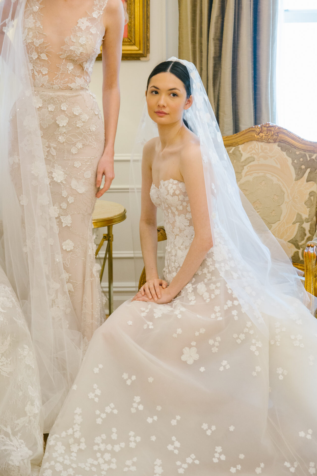Ness & Nessia in floral wedding gowns, elegant room.