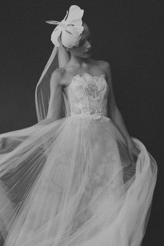 Woman in sheer strapless gown, butterfly headpiece, black and white.