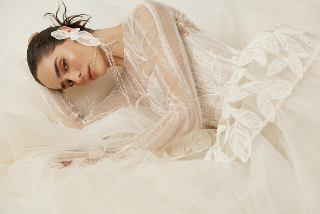 Woman in sheer leafy gown reclines, gazing softly.