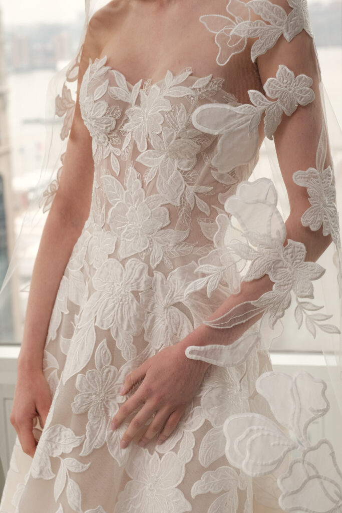 Woman in floral lace off-shoulder wedding dress indoors.