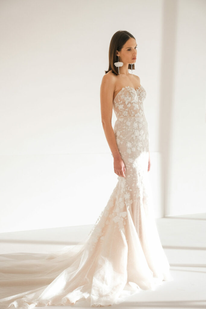 Woman in floral-lace wedding gown, sunlit room.