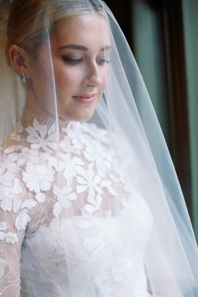 Bride in floral Mira Zwillinger gown by sunlit window.