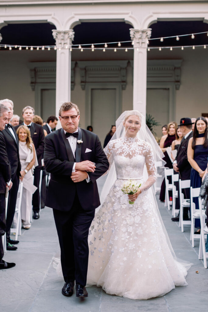Bride Katya Ruiz in couture gown walks outdoor aisle.