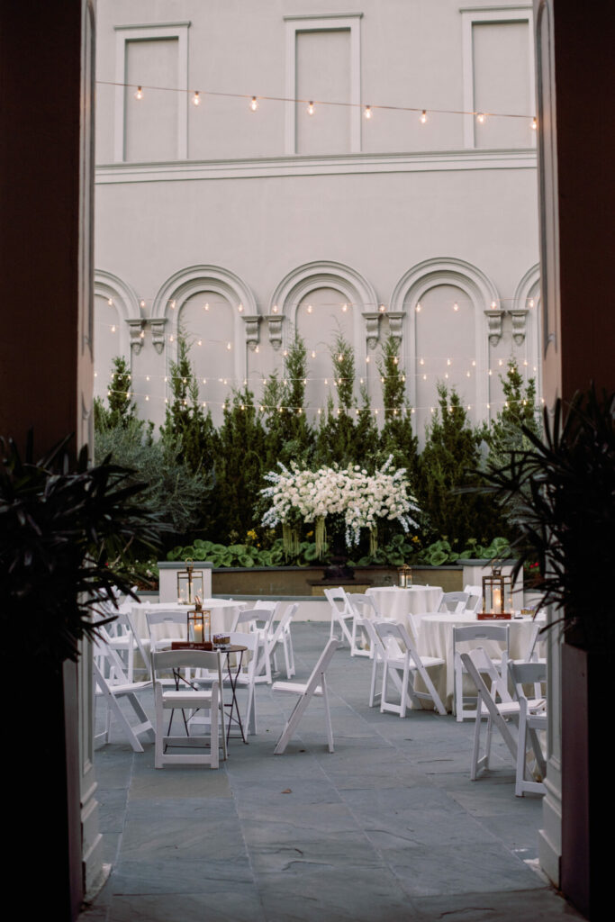 Elegant courtyard event setup with florals and string lights.