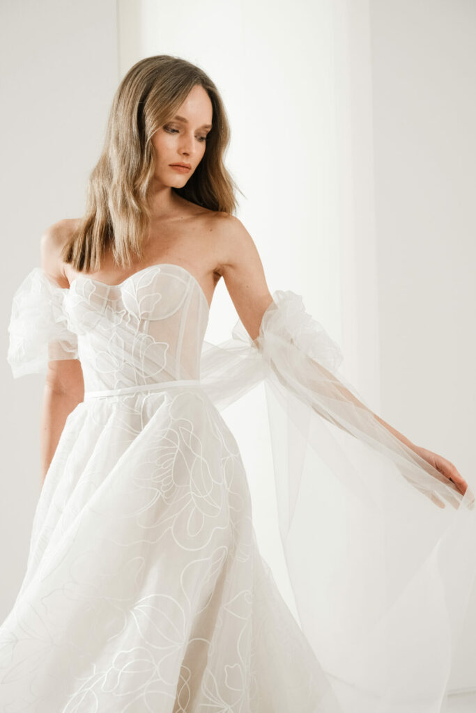 Woman in white off-shoulder wedding dress, looking serene.