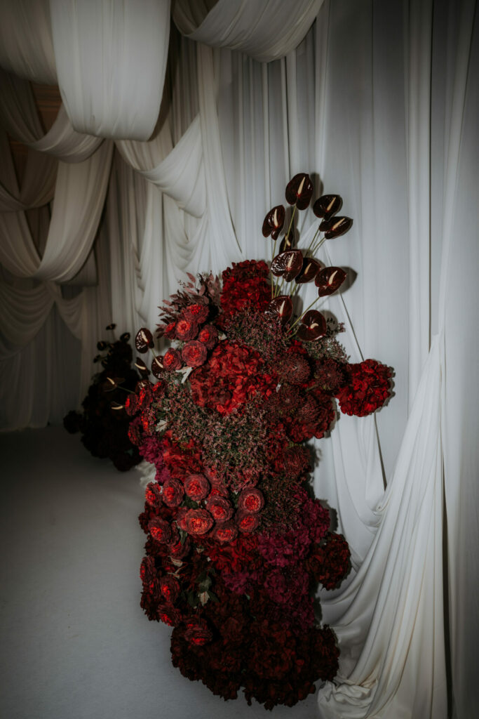Deep red roses and dark foliage against white drapes.